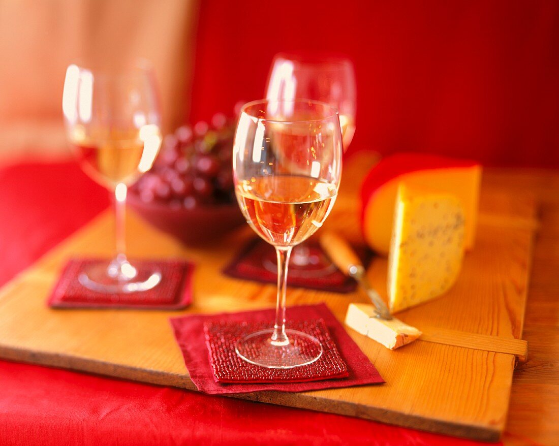 Glasses of White Wine on Red Coasters with Cheese and Grapes