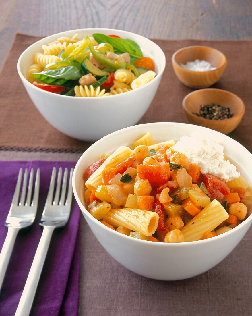 A Bowl of Rigatoni with Tomatoes, Carrots, Celery and Chickpeas and a Bowl of Fusilli Pasta Salad