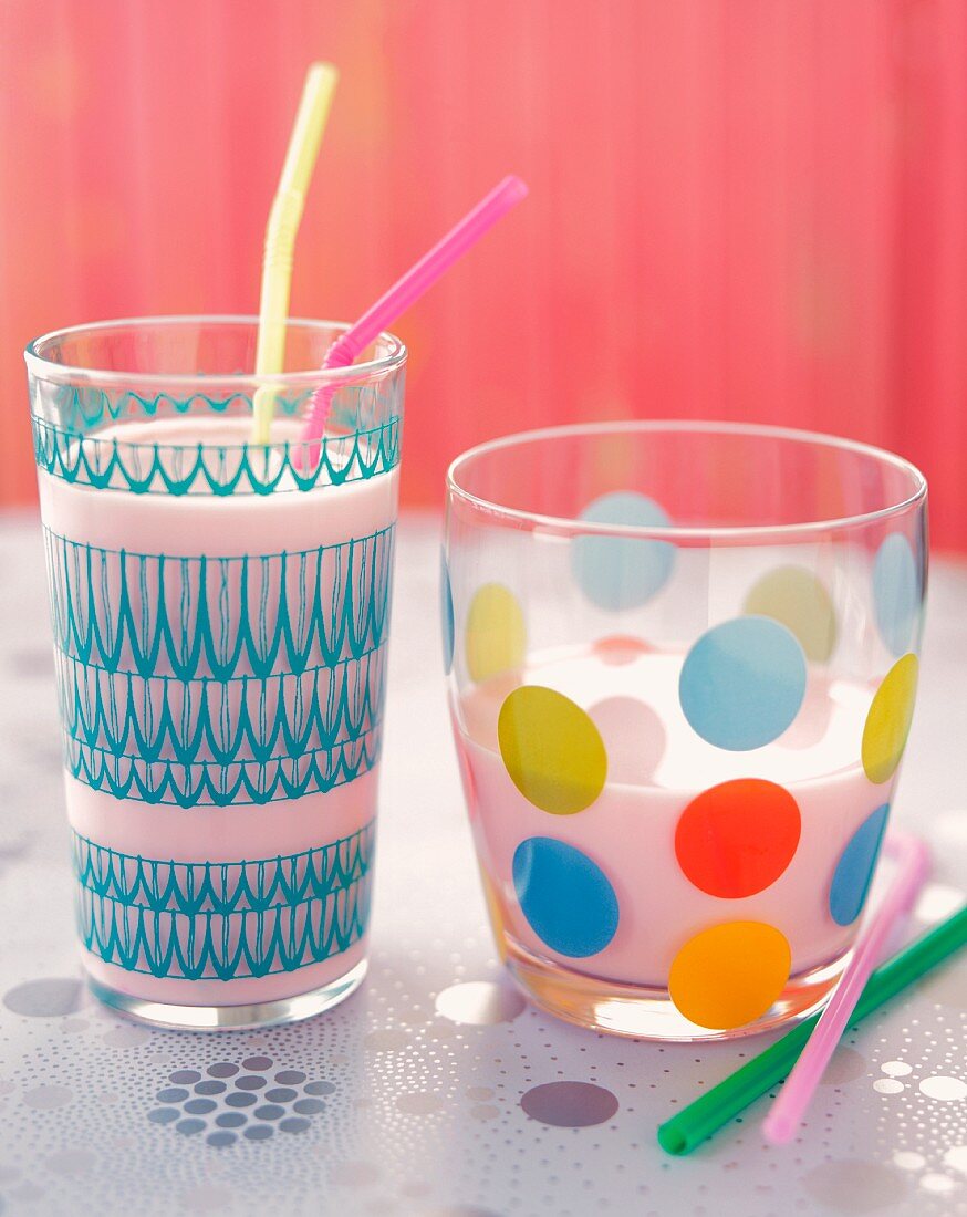 Two Colorful Glasses of Milk with Straws, One Full and One Half Full