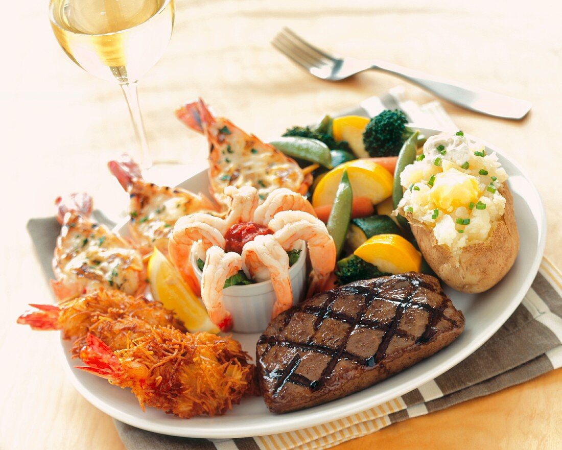 A Surf and Turf Platter with Grilled Steak, Three Types of Shrimp, Mixed Vegetables and Baked Potato