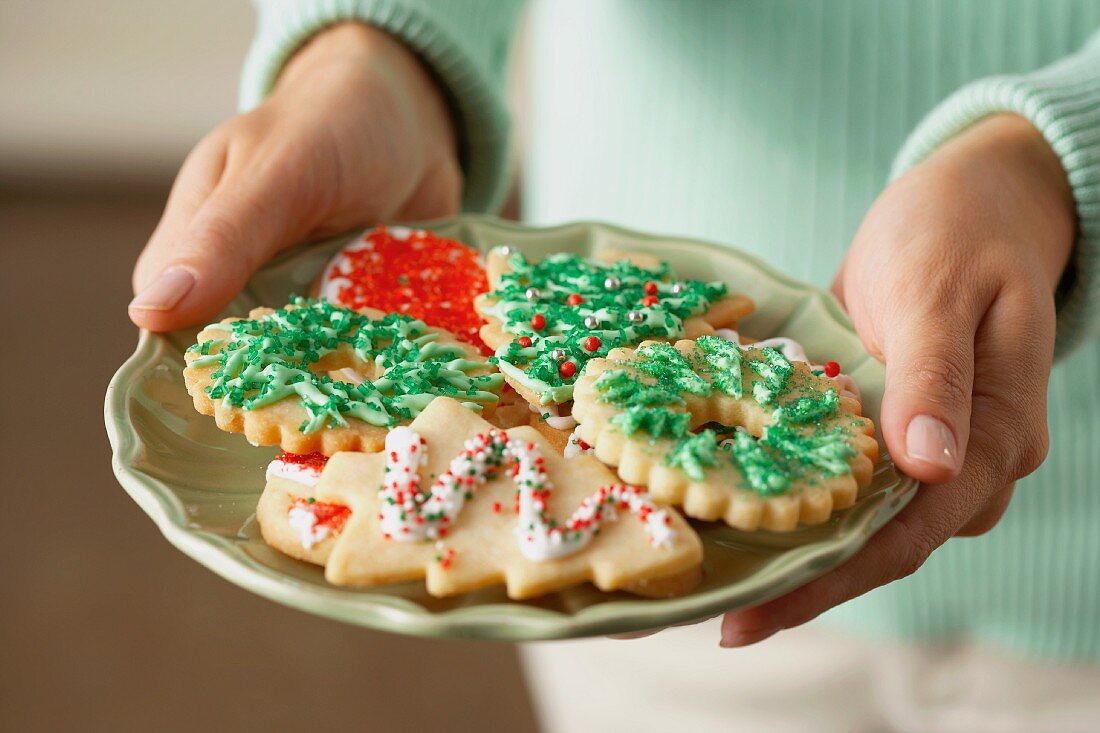 Hände halten Teller mit bunten Weihnachtsplätzchen