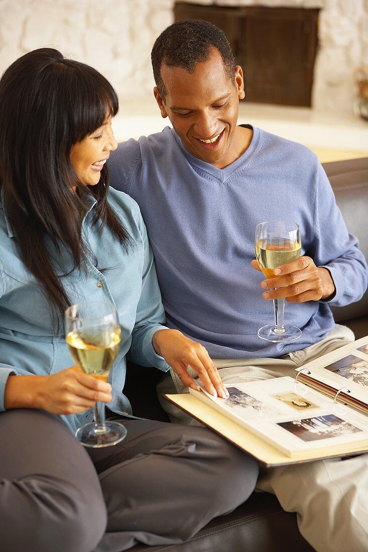 Paar auf dem Sofa trinkt Weißwein und blättert im Fotoalbum