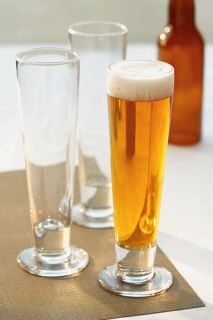 Glas helles Bier neben zwei leeren Biergläsern