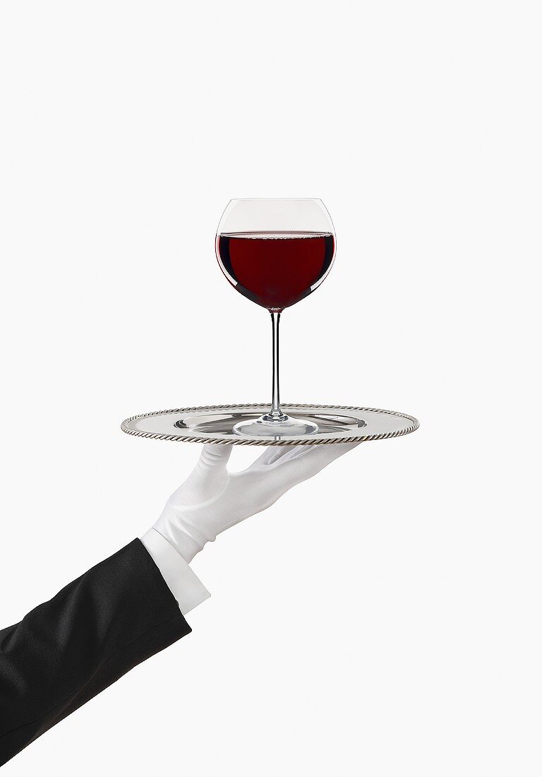 Hand mit weißem Handschuh hält Tablett mit Rotweinglas