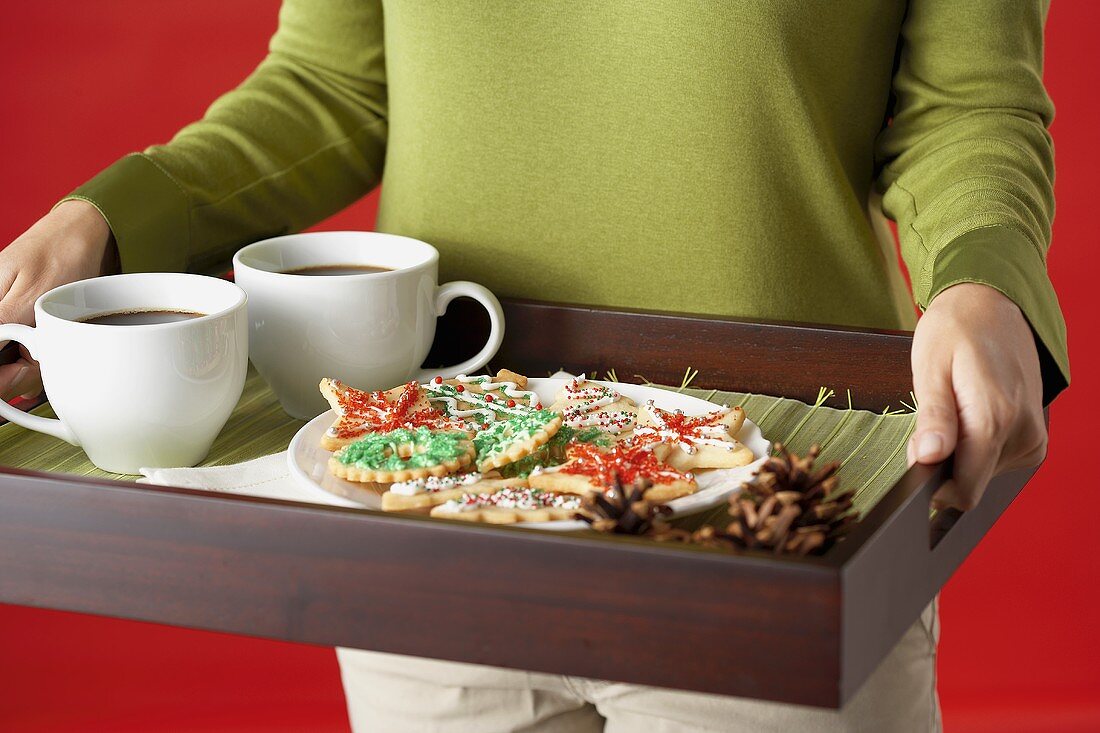 Frau serviert Tablett mit Weihnachtsplätzchen und Kaffee