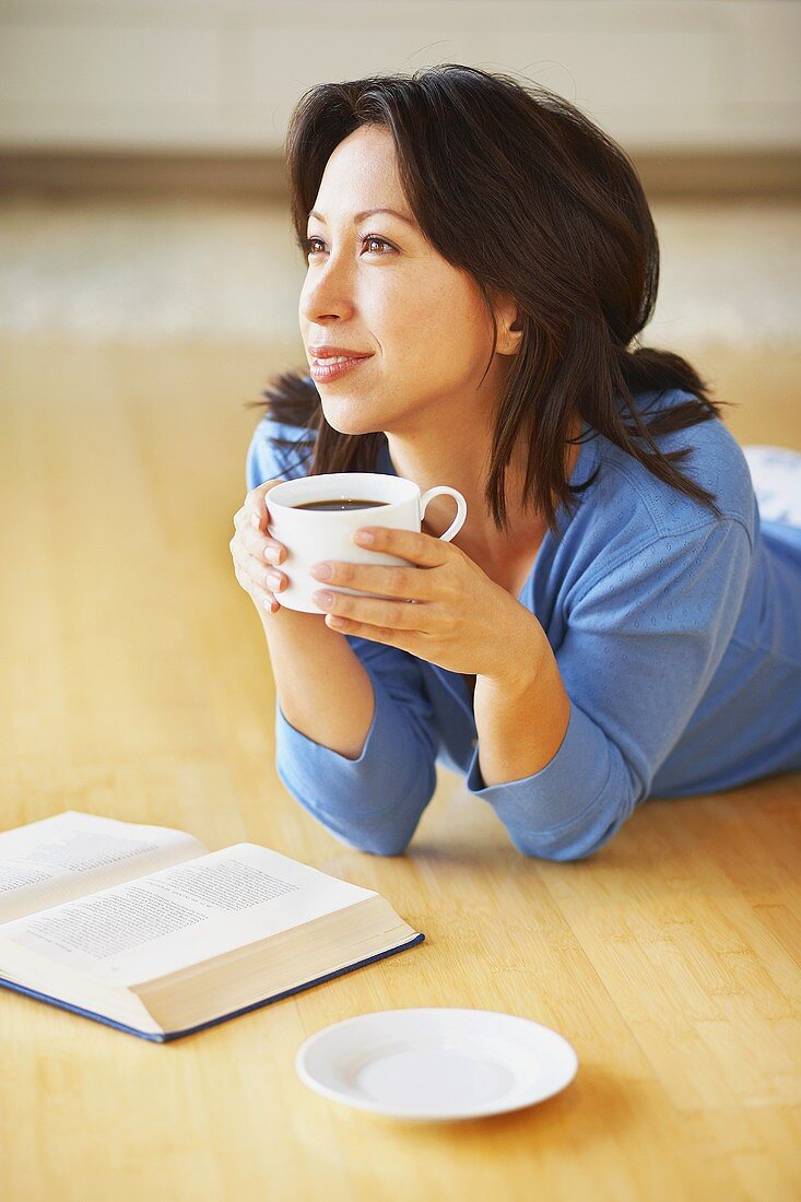 Frau mit Kaffee und Buch (auf dem Fussboden liegend)
