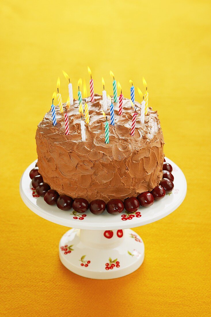 A Chocolate Cherry Birthday Cake with Lit Candles on a Cake Stand