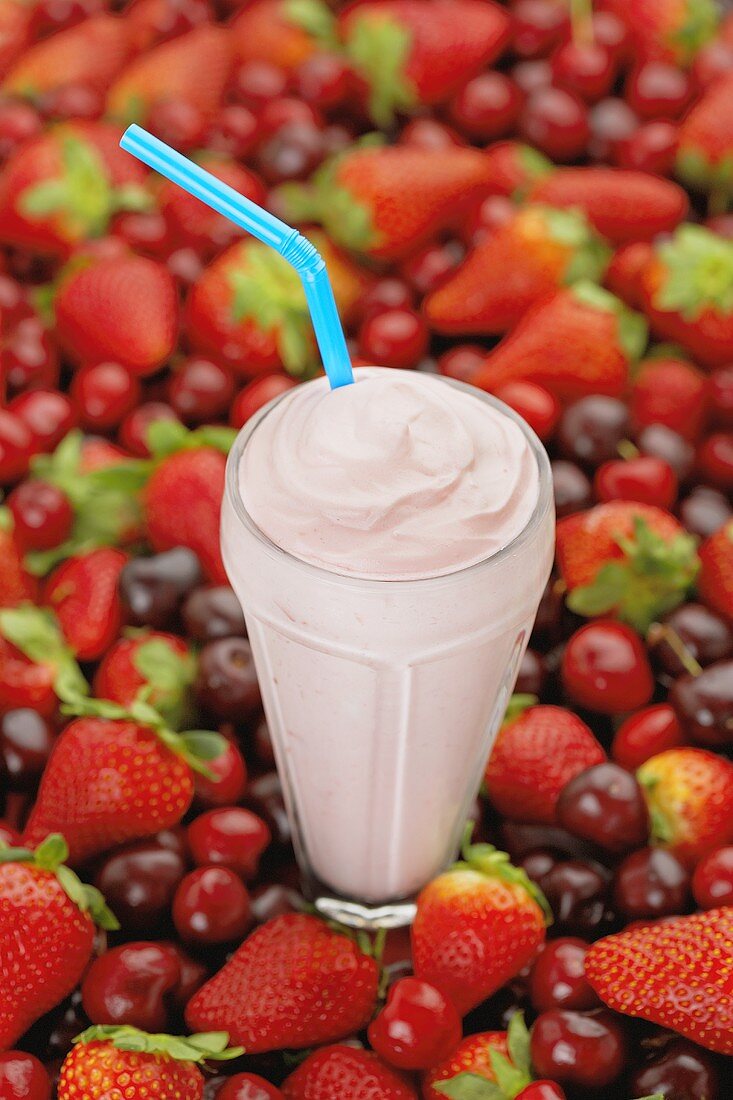 A Strawberry Shake with a Straw Surrounded by Strawberries and Cherries