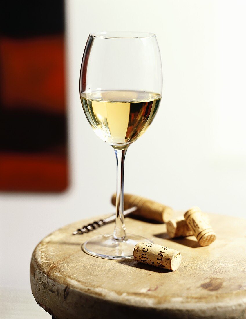 A Glass of White Wine with Corks and Corkscrew