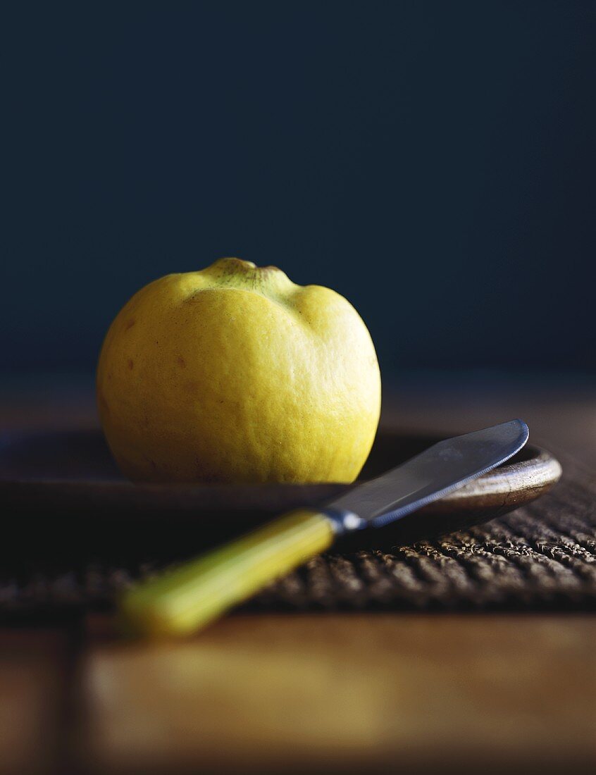 A Whole Quince on a Plate with a Knife