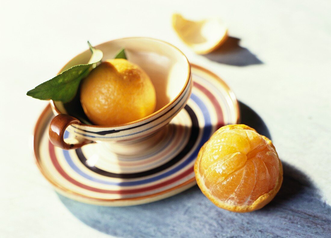 An Orange in and Next to a Striped Cup and Saucer