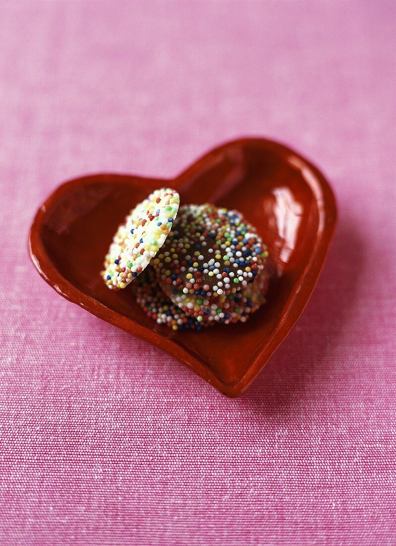 Schokoladenkonfekt mit bunten Zuckerperlen in roter Schale