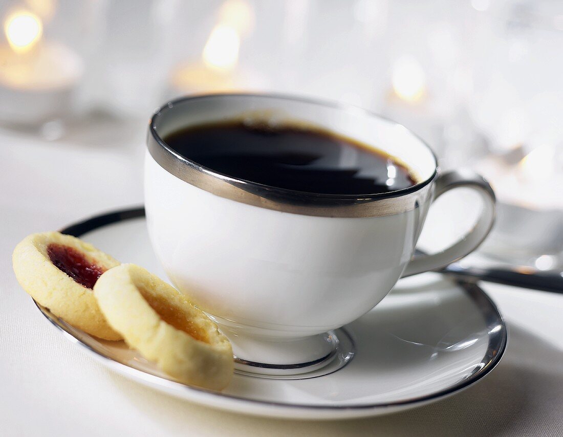 Tasse schwarzer Kaffee mit Marmeladenplätzchen auf Untertasse
