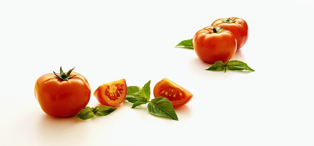 Whole and Sliced Tomatoes with Fresh Basil Leaves on a White Background