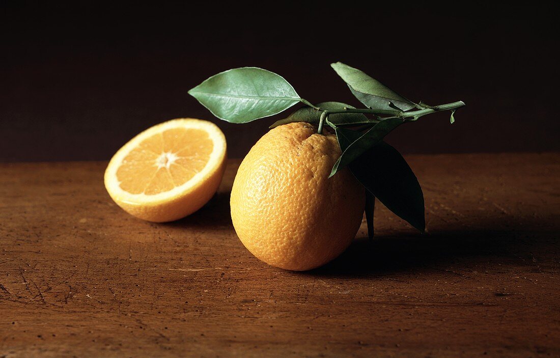 A Whole and Halved Orange with Leaves on Wood