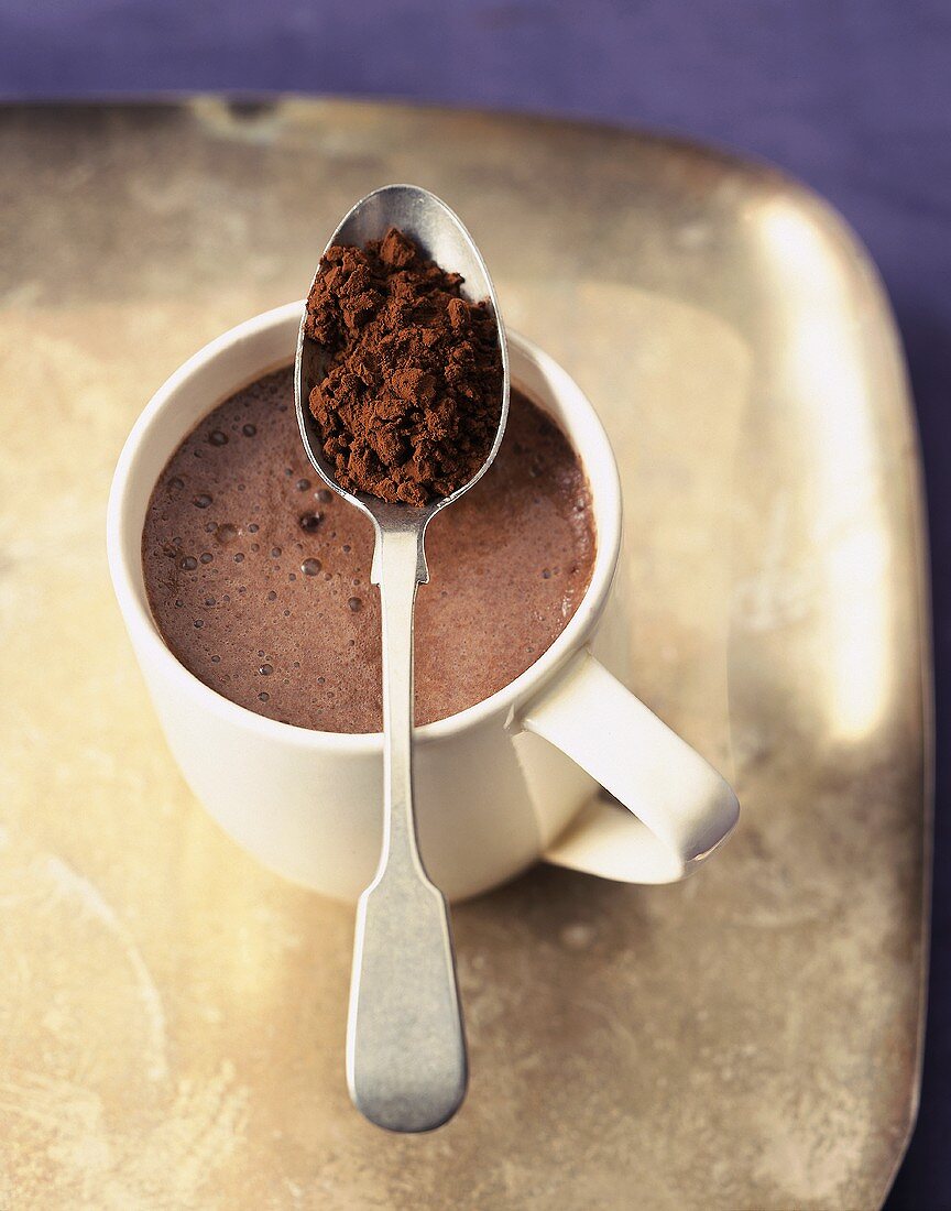 A Cup of Hot Cocoa on a Tray with Spoonful of Cocoa Powder