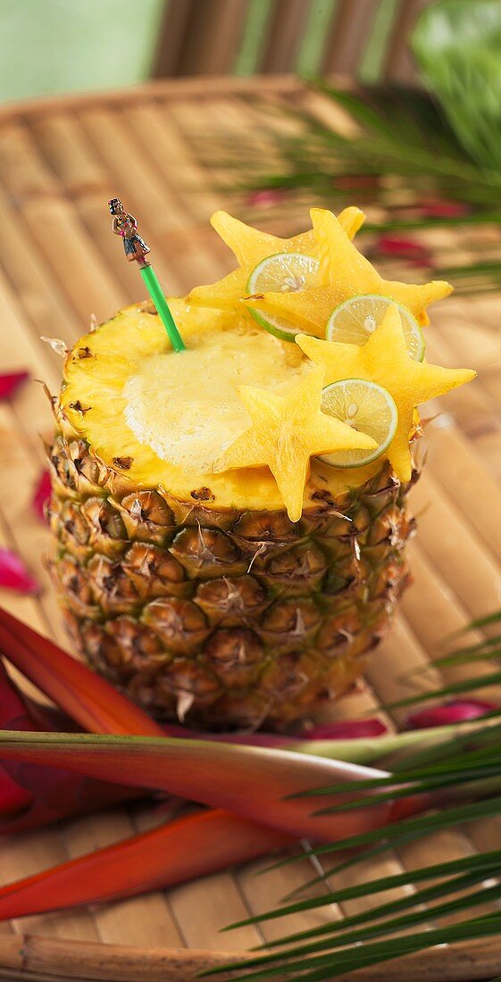 Tiki Pineapple Drink Served in Pineapple on Bamboo Table; Tropical Flowers
