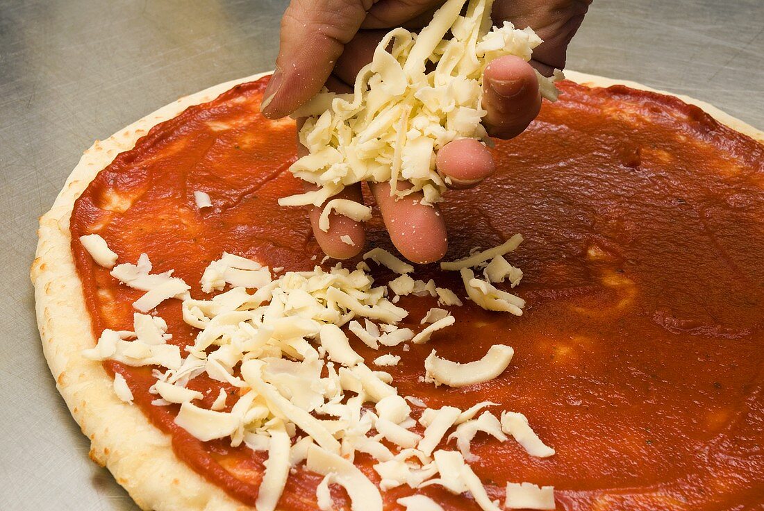 Hand bestreut Pizzaboden mit geriebenem Käse