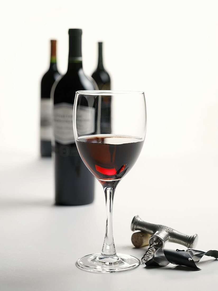 A Glass of Red Wine with Corkscrew, Cork and Wine Bottles