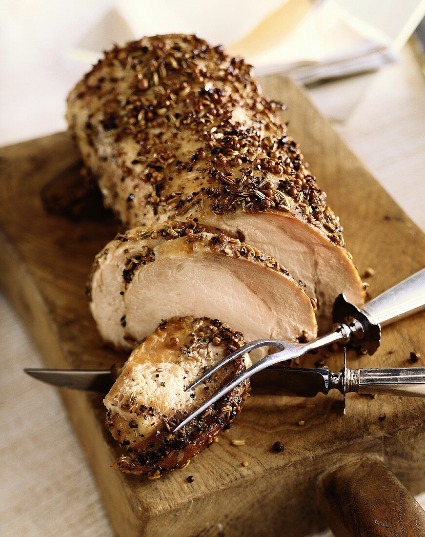 Partially Sliced Herb Crusted Pork Loin on Cutting Board with Serving Utensils