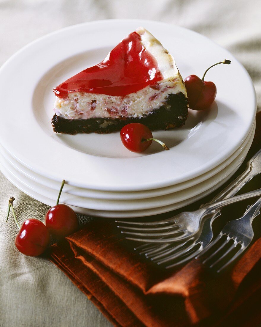 Slice of Cherry Cheesecake with a Brownie Crust and Cherry Topping on White Plate; Cherries