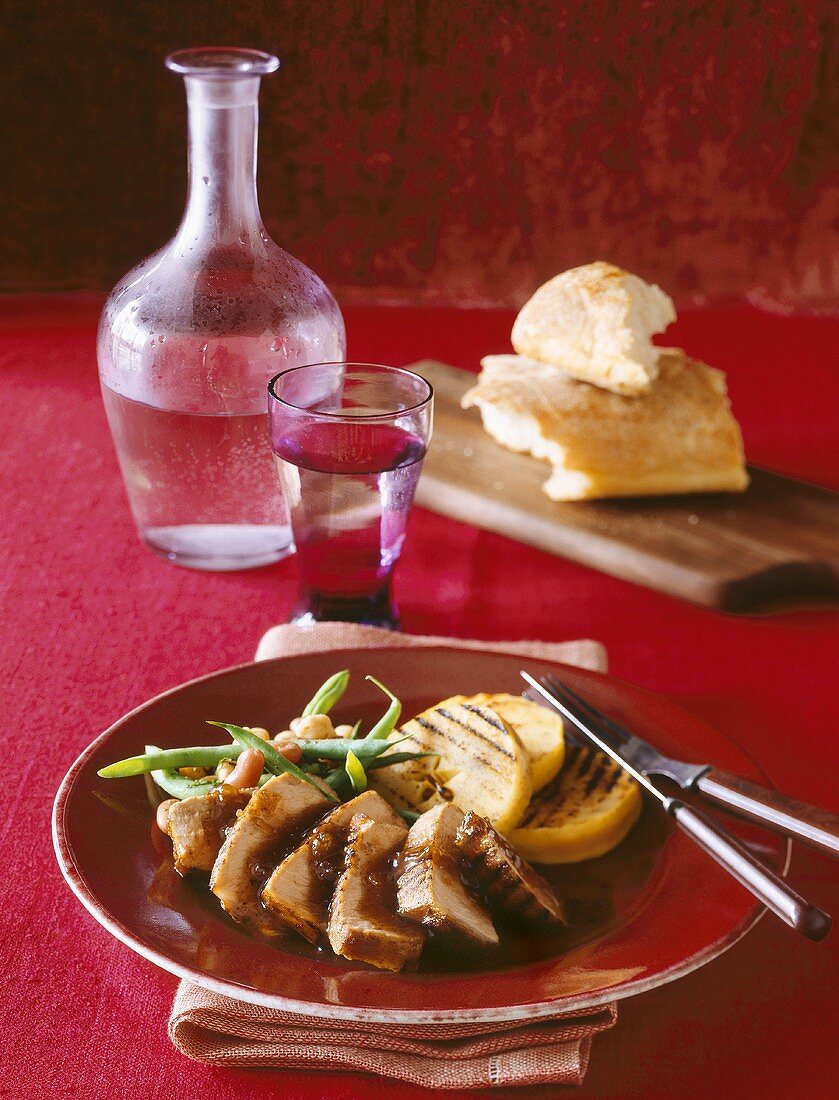 Serving of Sliced Grilled Pork with Grilled Polenta Slices and Green Beans; Glass of Water