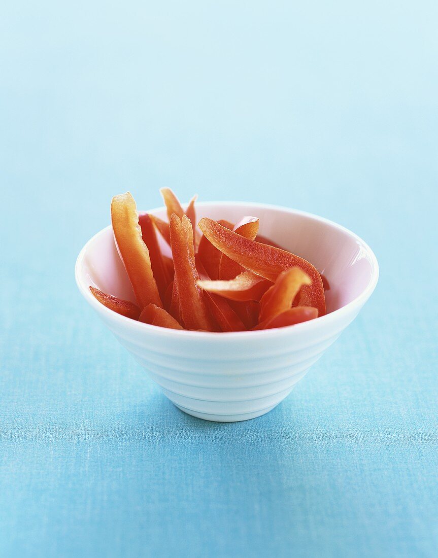 Red Pepper Strips in a White Bowl on a Blue Background