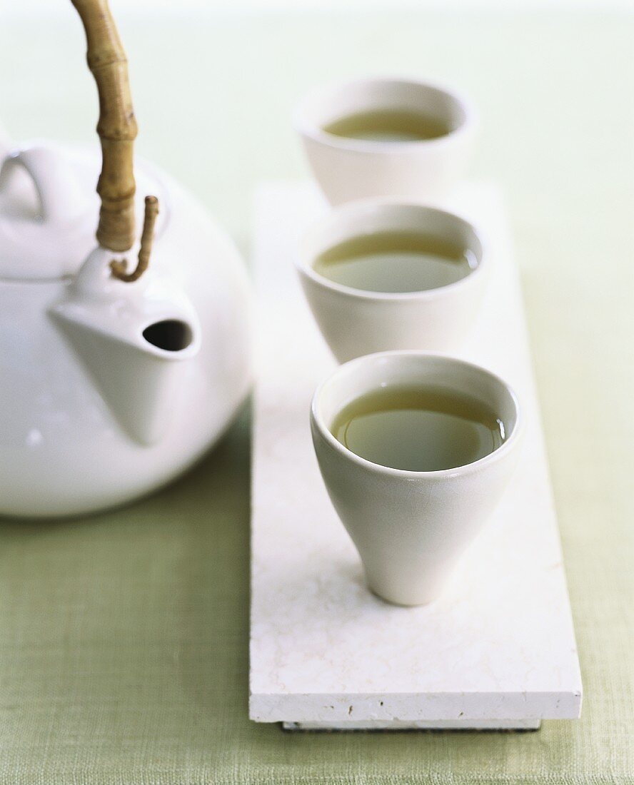 Grüner Tee in drei Schälchen neben Teekanne