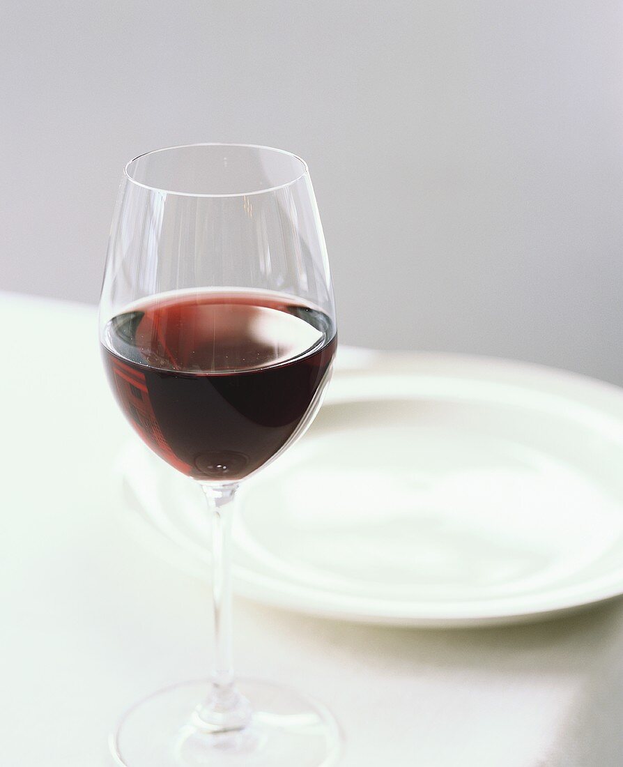 Glas Rotwein auf weiss gedecktem Tisch