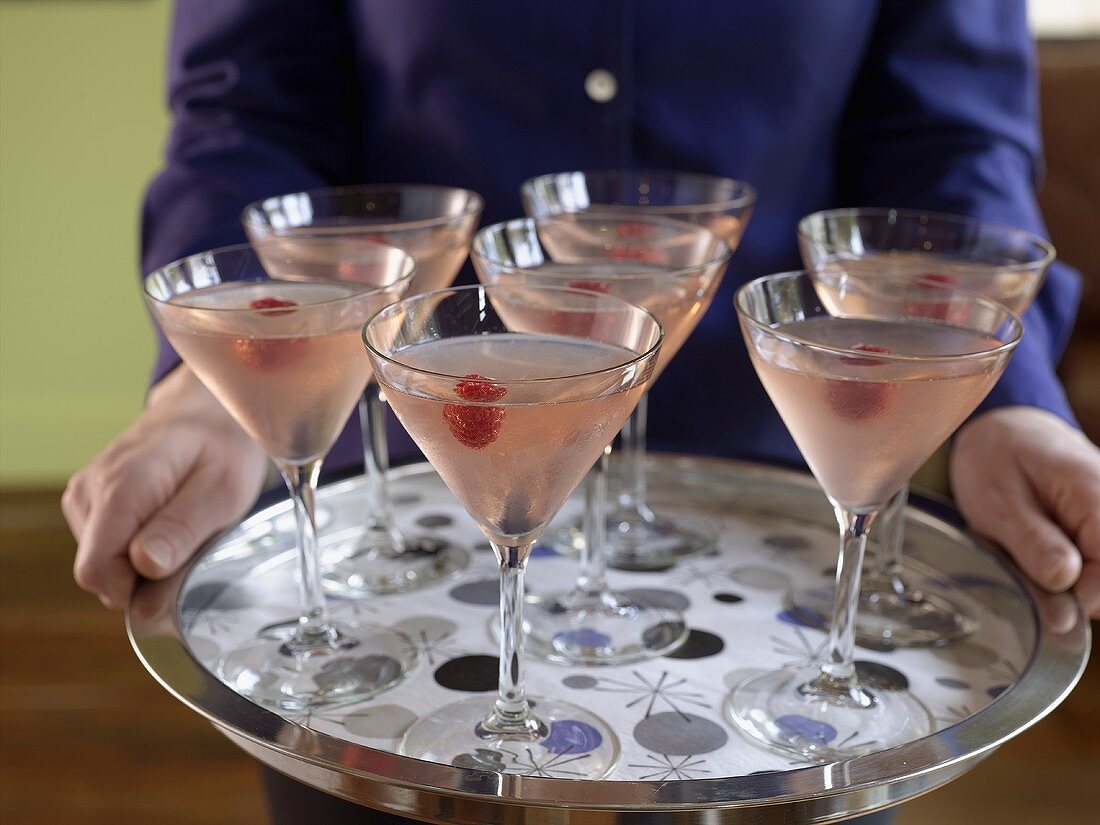 Person holding a silver tray of raspberry Martinis
