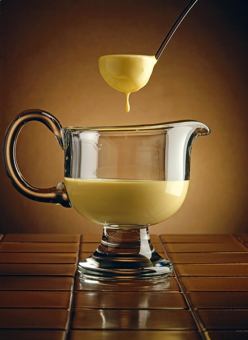 Ladle Scooping Hollandaise Sauce From Glass Sauce Dish