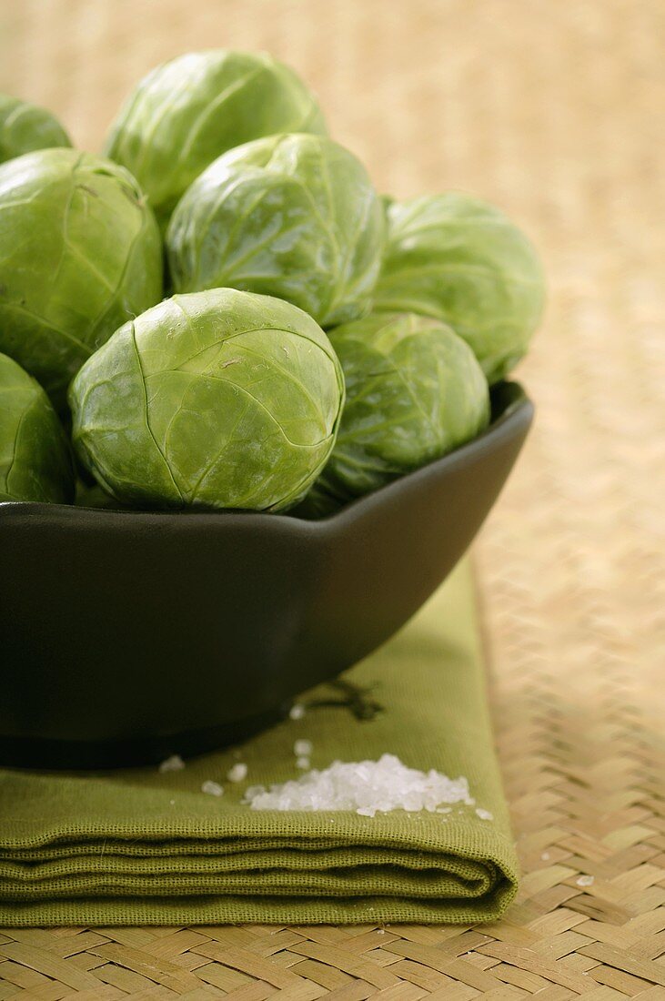 Black Bowl of Brussel Sprouts on a Folded Green Cloth with Sea Salt