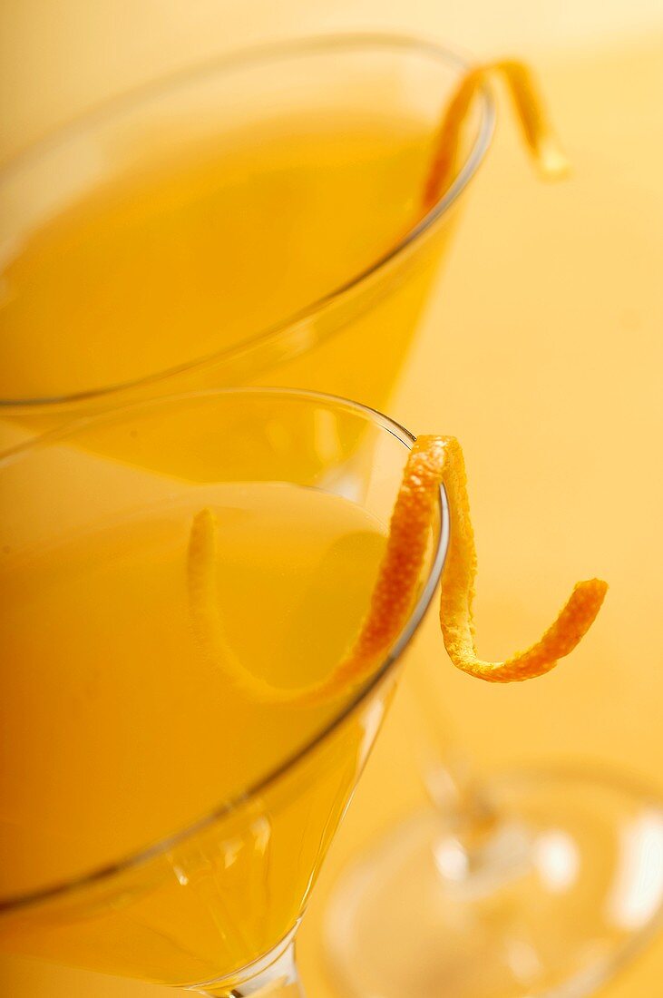 Two Citrus Martinis Garnished with Orange Zest on an Orange Background