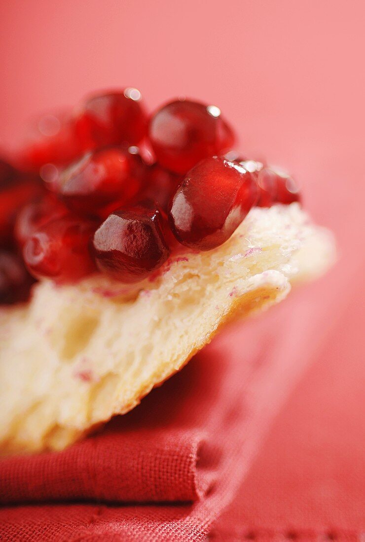 Fresh Pomegranate Seeds on a Slice of Crusty Bread; Red Background