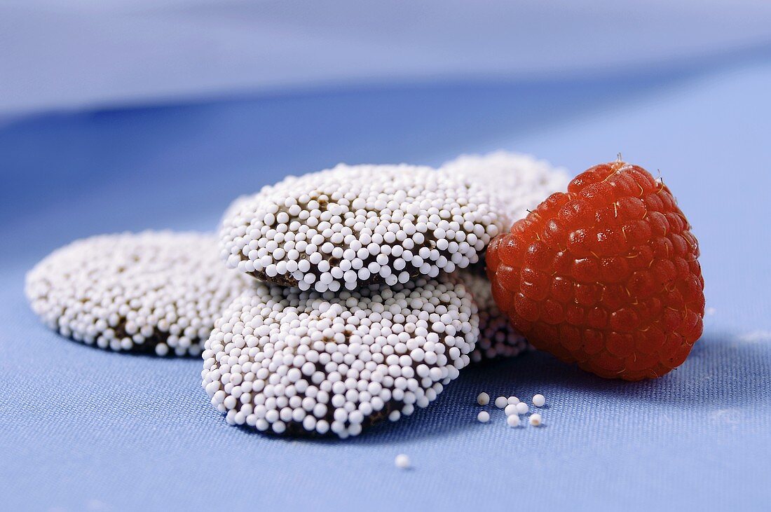 Small Pile of Non-Pareils with a Red Raspberry on Blue Background