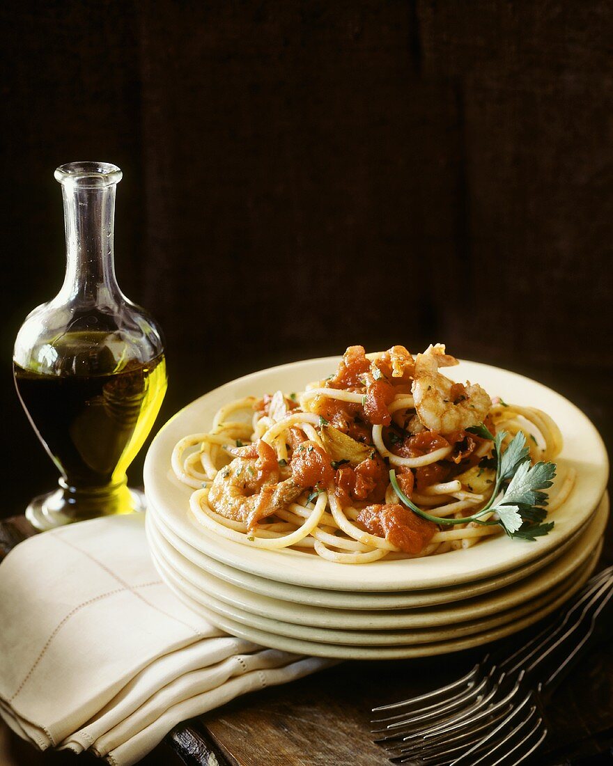 Spaghetti mit Garnelen und Tomaten, dahinter Olivenöl