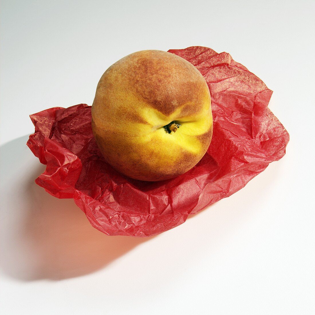 A Single Peach on Red Tissue Paper on White Background