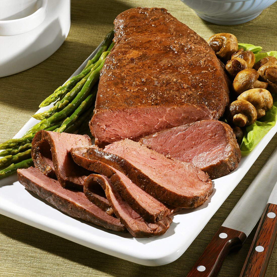 Partially Sliced London Broil on a Platter with Asparagus and Mushrooms