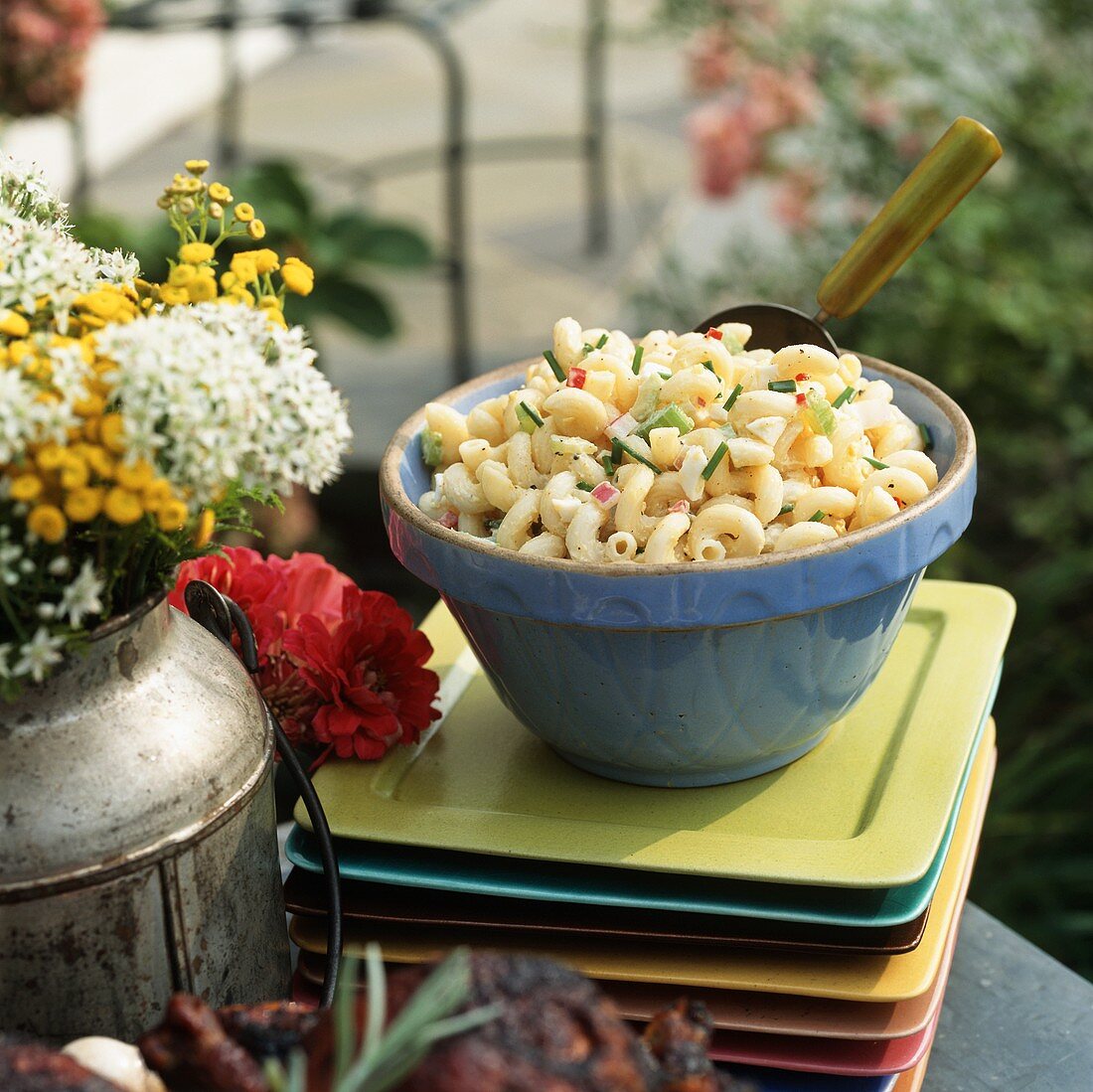 Pasta salad in blue bowl on pile of plates (outdoors)