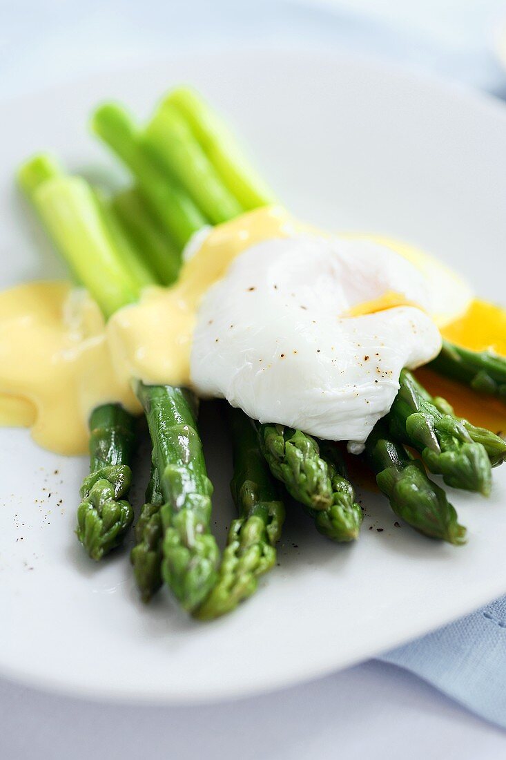 Poached Egg with Hollandaise Sauce Over Asparagus on White Plate
