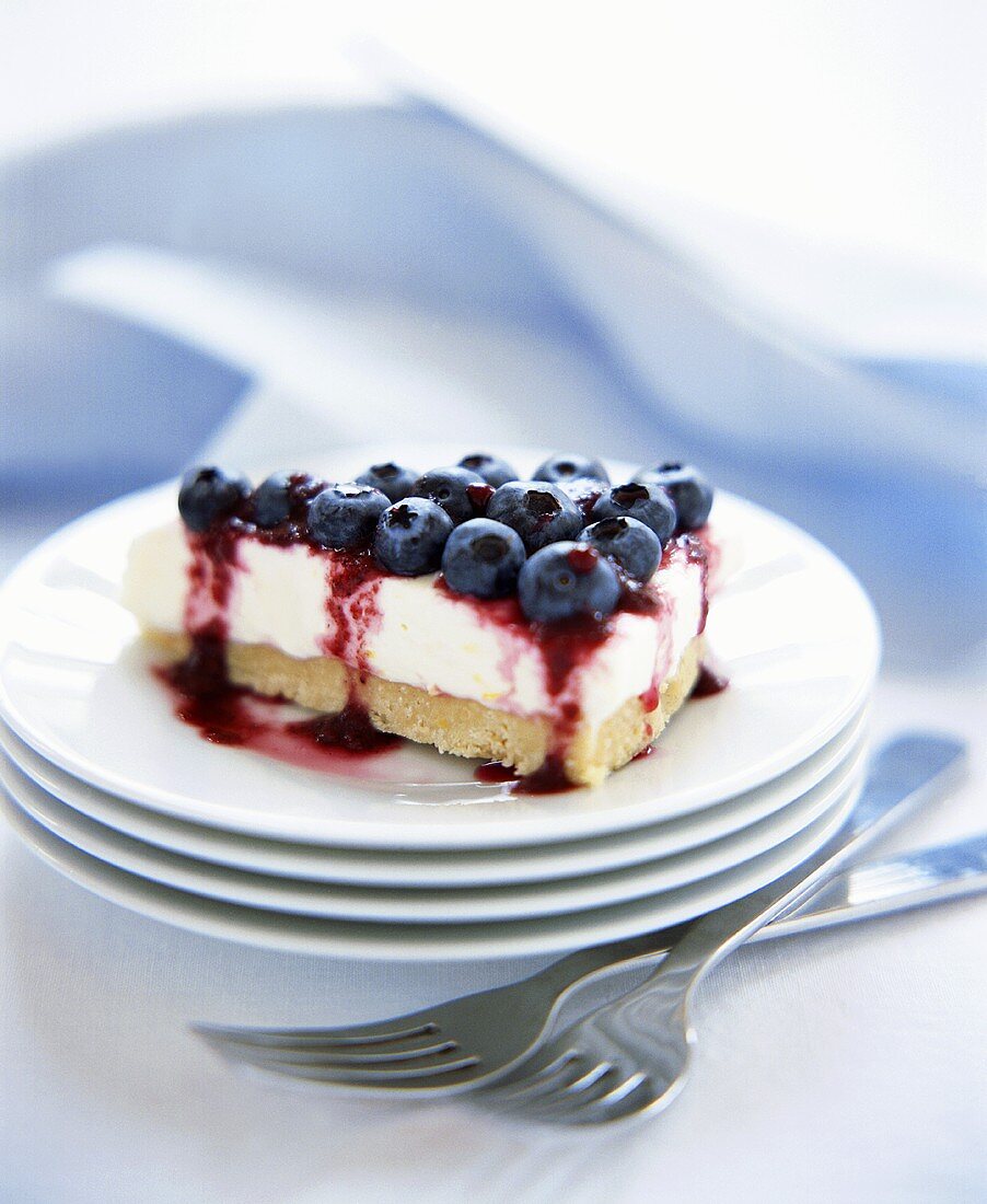 Slice of Cheesecake with Blueberry Topping on Stack of White Plates, Forks