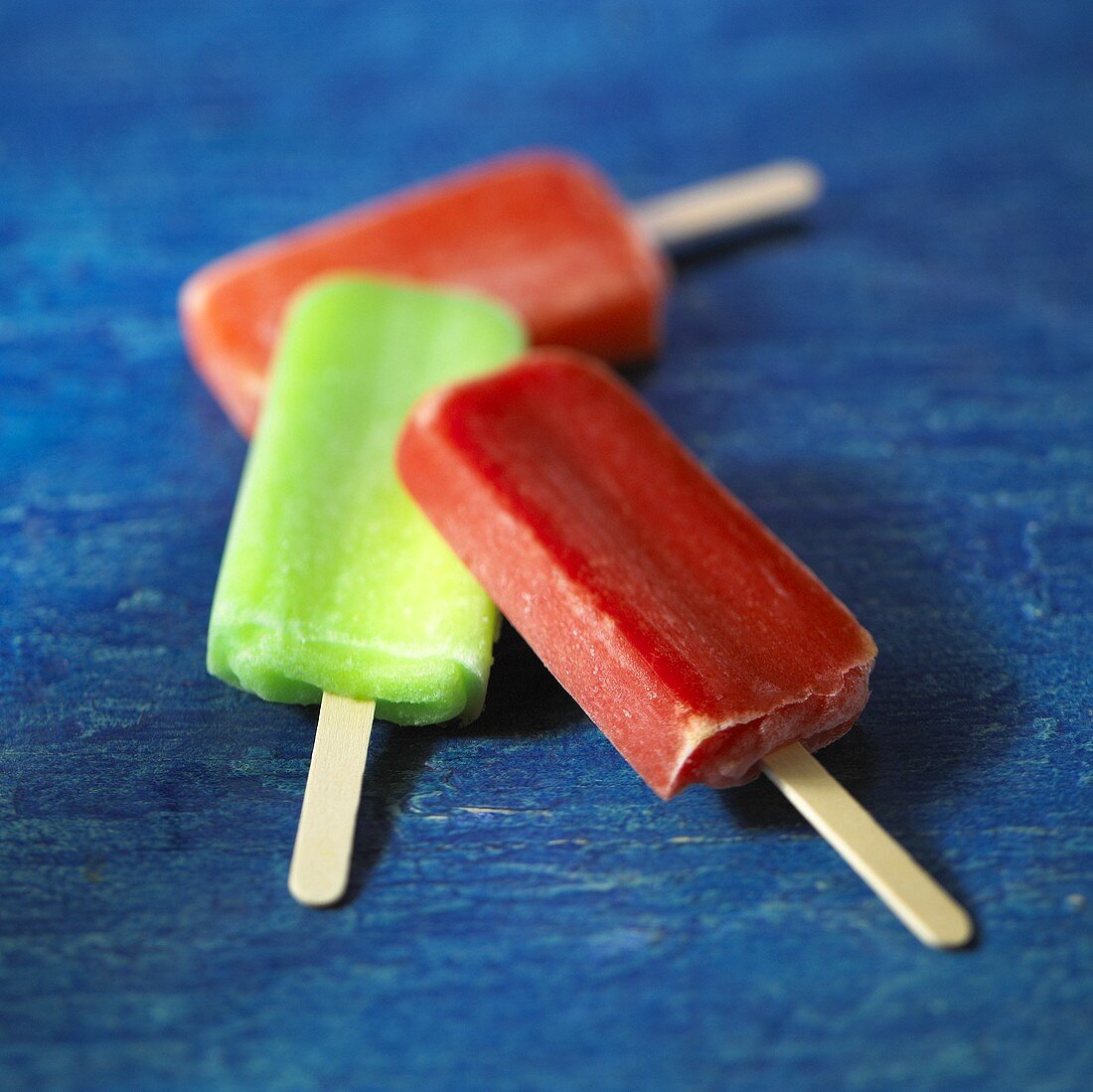 Three Fruit Flavored Popsicles on Blue Background