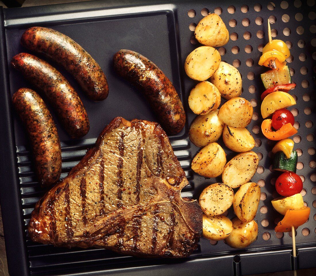Grillrost mit Steak, Würstchen, Kartoffeln und Gemüsespiess