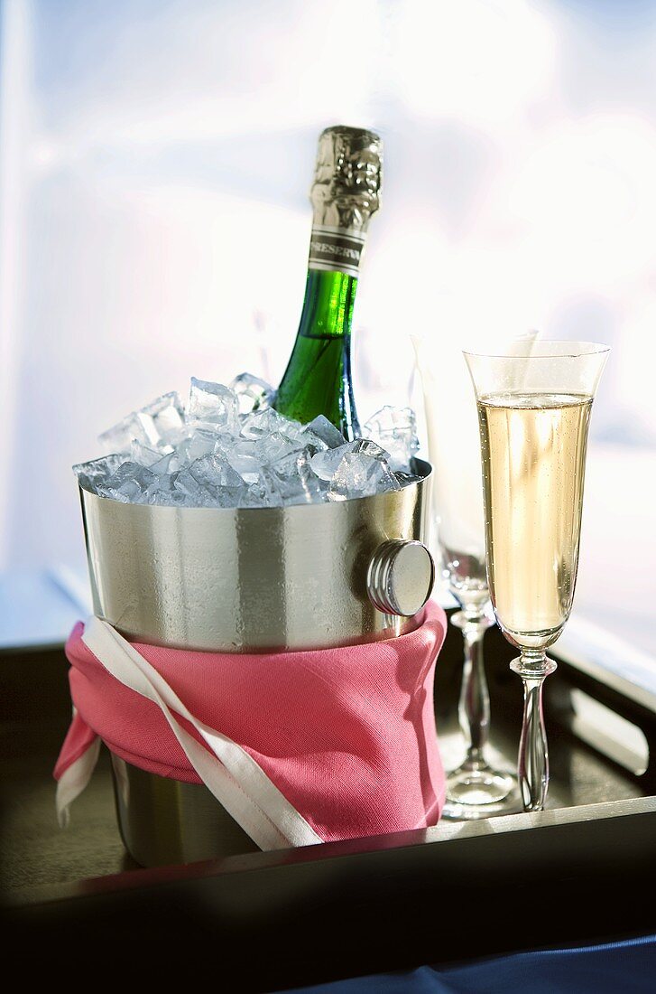 Bottle of sparkling wine in champagne bucket, glasses on tray