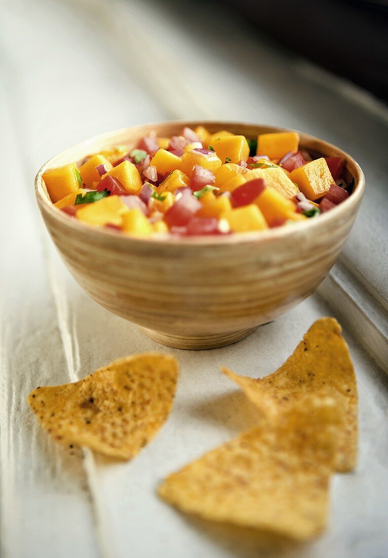 Mango salsa in bowl, tortilla chips beside it