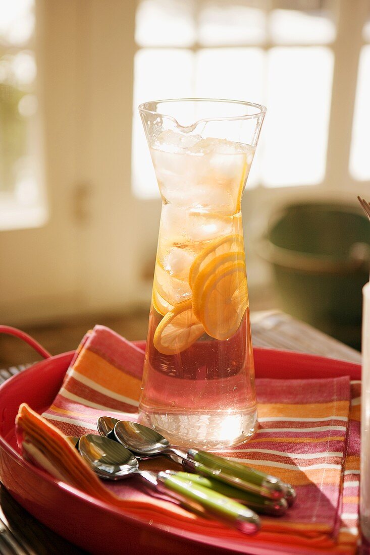 Iced water with lemon slices in carafe, spoons beside it