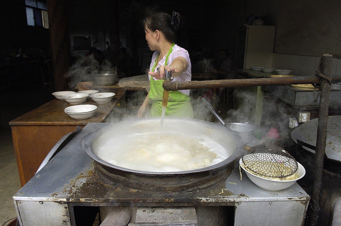 Asiatische Frau giesst Wasser in grossen Kessel