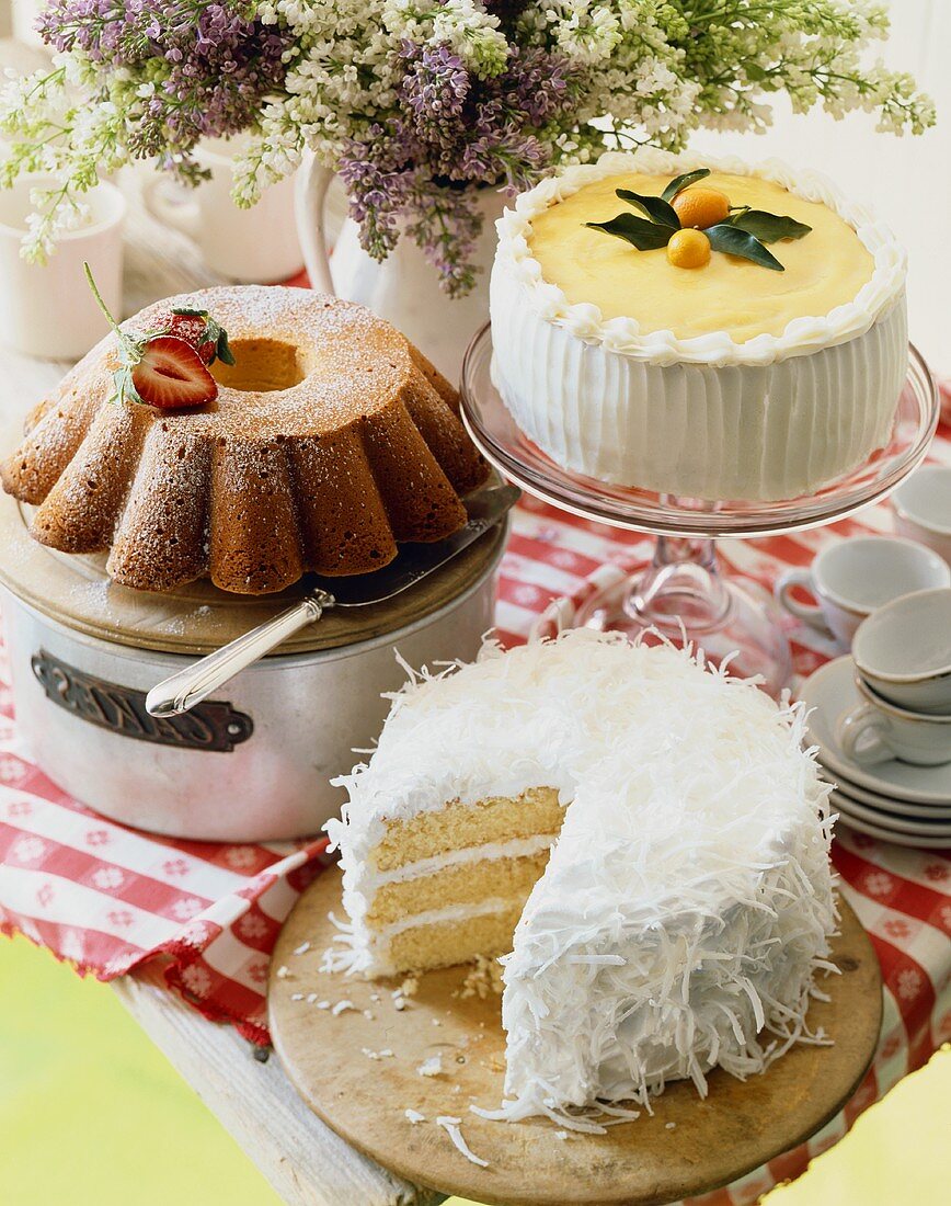 Three Assorted Cakes on a Table with Tea Cups and Saucers