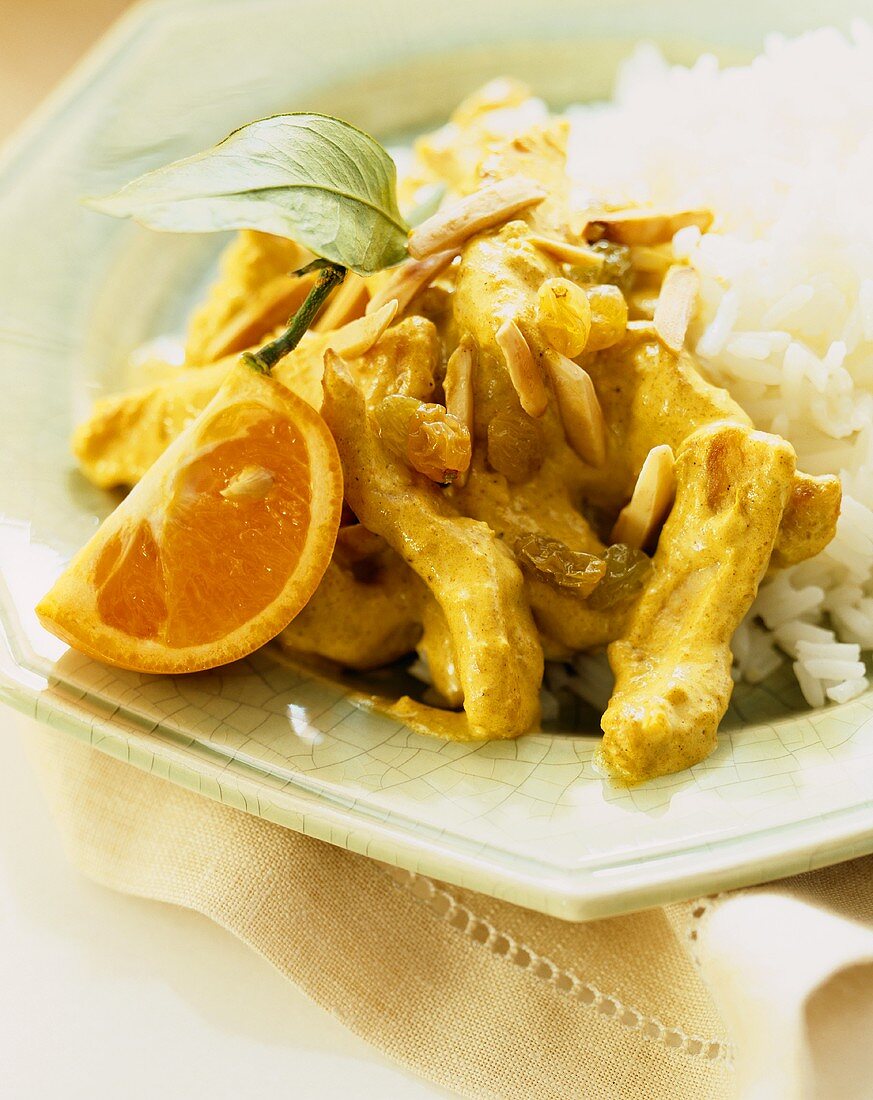 Curried Chicken with Almonds and Golden Raisins Over Rice; Orange Wedge Garnish