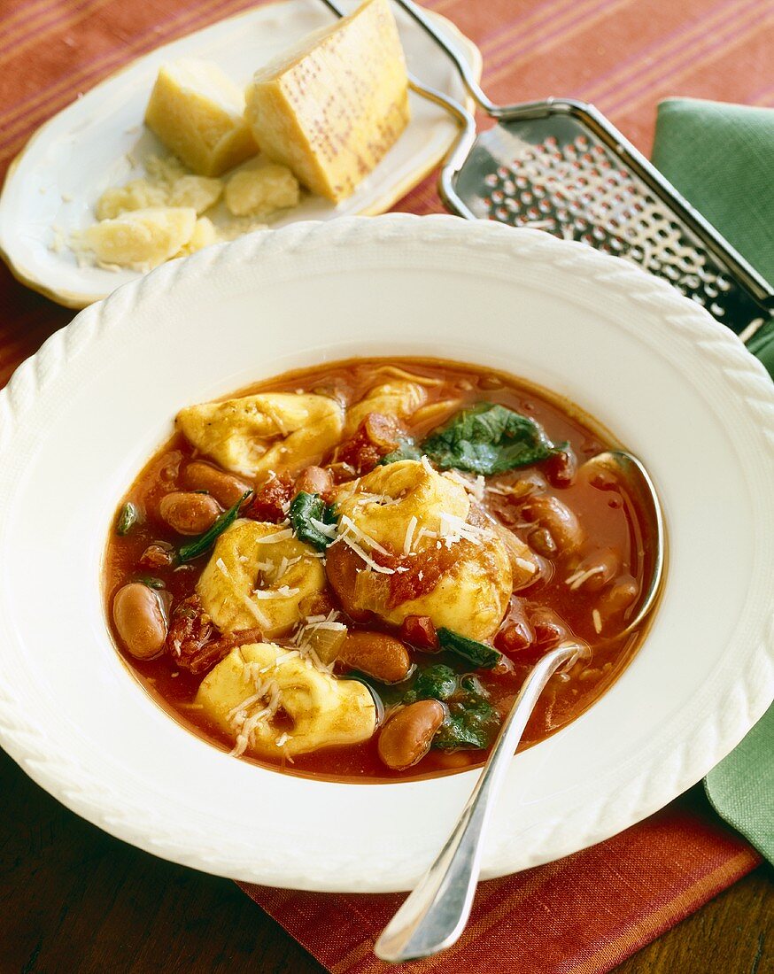 White Bowl of Tortellini Tomato Soup with a Spoon; Parmesan Cheese and Cheese Grater